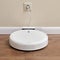 White robotic vacuum cleaner is charged from an electrical outlet on the base, wooden laminate