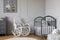 White rocking chair with pillow next to wooden cradle in elegant baby room with duck`s poster on the wall