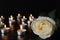 White rose and blurred burning candles on table in darkness, closeup. Funeral symbol