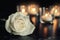 White rose and blurred burning candles on table in darkness, space for text.