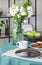 White rose in glass vase next to coffee mug and big plate on dining table