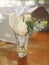 White roses in a transparent glass on a polished wooden table