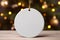 A white round ceramic Christmas ornament. Festive decoration for mockup. Blurred green tree with lights in the background