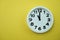 White round clock showing eleven o`clock on yellow background