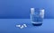 White round medical pills, vitamins, in the distance there is a beautiful blue glass with clean water.