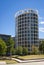 A white round multi-storey building with lots of windows, grass lawn and green trees grow in front of it.