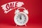 White round plastic alarm clock on a red background and the inscription Sale. Black Friday concept, sale season, copy