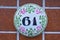 A white, round shaped house number plaque on tile, showing the number sixty one