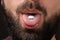 white round tablet on tongue of open mouth of bearded man with dark mustache on black background, take vitamins