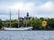 White sailboat on the background of green trees and beautiful buildings of Stockholm Sweden