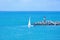 A white sailboat sails on the sea near the lighthouse and breakwater on a summer day. Picturesque seascape.