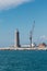 White Sailboat in the Sea and Crane at Work in Boatyard