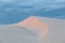 White sand dune under cloudy sunset skies.