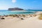 The white sand beside the sea, where the bottom can be seen, the beach with people. Beautiful mountains on a blue horizon.