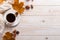 White scarf, cup of coffee and dry yellow leaves on a wooden table. Autumn mood, copy space