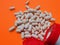 White scattered pills and white jar with red lid on orange background. Selective focus. The concept of dietary supplements