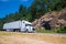 White semi truck trailer going highway with rocks green trees