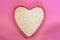 White sesame seeds in the shape of a heart on a pink background, top view. Super food ingredient. Healthy vegan concept