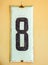 White Shabby Metal Plate With Black Number Eight, Nailed On Yellowewashed Wall