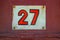 White Shabby Metal Plate With Red Number Twenty Seven Nailed On Red Metal Door