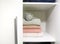 White shelf of the home wardrobe with colorful sweaters, jumpers and warm headphones. Small space organization