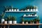 White shelves with decorative potted green plants and vase with dried flowers on blue colored wall in light room