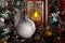 White shiny ball hanging on a branch of a Christmas tree against a red lantern with a candle