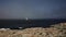 A white ship with a sail moves across the blue sea in a fog view from the ocean shore.