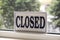 White sign with closed written on it with blurred trees on the background