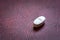 White single pill on a dark burgundy background, close up