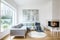 White sitting room interior with corner grey sofa, tulips in vase placed on end table, fireplace and modern art painting