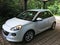 White small German car opel adam under carport in front of green trees and hedges