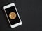 White smartphone and gold coin bitcoin on a black textural background.