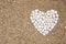 White smooth pebble romantic heart shape on sunny sand beach top view