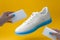 white sneakers with blue sole and female hands with sponges on a yellow background , shoes care concept