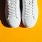 White sneakers on an orange background with hard shadows.