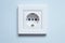 White socket with grounding contacts on a blue wall background. Electricity consumption concept