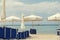 White solar umbrellas and blue beach chairs on a beach in Greece White sailboat on the horizon