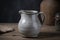 A white speckled ceramic pitcher with a curved handle and a spout, empty and the main focus, on a wooden table with a dark and