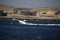 A white speed boat on the Mediterranean sea leaving a trail of sea spray behind it.