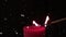 White spots floating against match stick lighting a red candle against black background