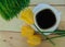 A white square cup of coffee three yellow tulips and green sprouted wheat