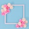 White square shaped picture frame surrounded by pink and white foam rose flower blossoms on blue background