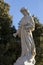 White stone angel grave marker in a cemetary against a tree background