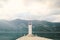 White stone lighthouse with a red lantern, in the center of the frame against a background of mountains, on the island