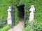 White stone sculptures at the entrance to the garden maze in Hever Castle park and black metal patterned gates on a blurred