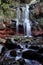 White stream of water flows over a wet, overgrown stone face