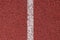 White strip of markings on a red background of rubberized cover of sports grounds and stadiums for outdoor use. Red and white reli