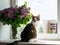 A white-striped cat sits on a windowsill next to a bouquet of lilacs