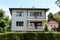 White suburban family house with two front balconies and open windows surrounded with hedge and trees